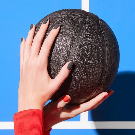 Hands holding a black basketball with one hand’s nails painted in the shade climbing high and the other in the shade start signs only