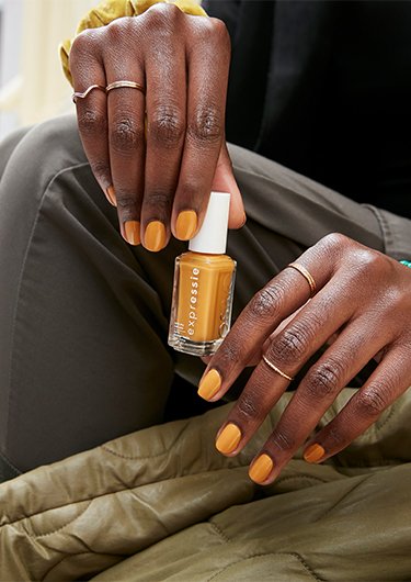 Model with dark skin and orange nails painted with essie nail polish sitting on a city street