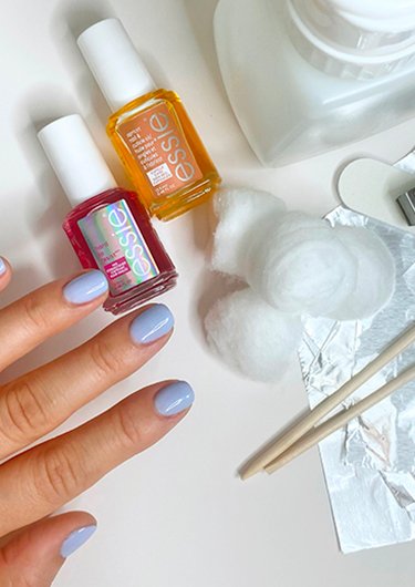 hand with purple gel nail polish next to nail tools and essie nail care products 