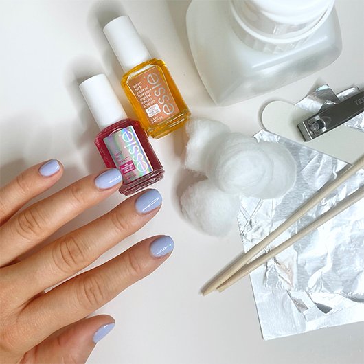 hand with purple gel nail polish next to nail tools and essie nail care products 