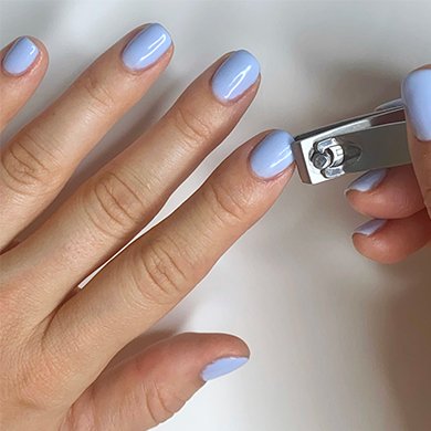 trimming fingernail with purple gel nail polish using a nail clipper