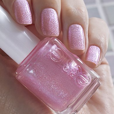Model wearing pink sparkling nail topper holding feel the fizzle essie nail topper bottle.