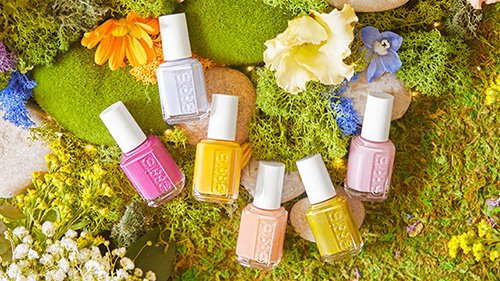 6 bottles of nail polish laid down on a mossy ground with mossy rocks and flowers