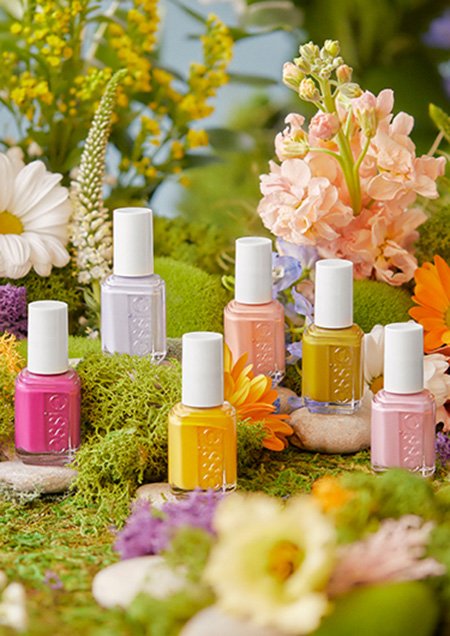 Six nail polish bottles displayed among mossy stones and flowers