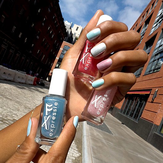 Closeup of dark skin model holding 3 bottles of essie expressie fx nail polish.