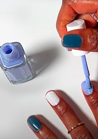 Dark skin model applying lilac essie expressie nail polish with an open bottle on the left